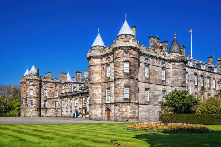 the rustic Holyrood Palace against a blue sky background and a lush green lawn