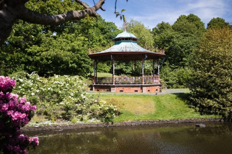 A gazebo surrounded by flowers and lush green foliage with a lake below in Sefton Park