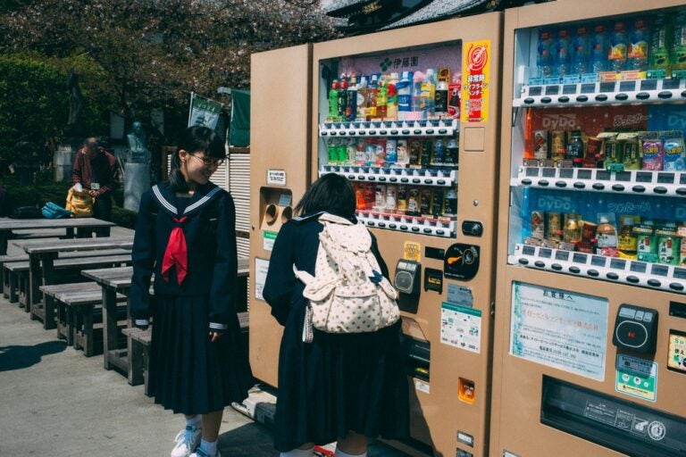 two young women at a vending machine in japan filled with cold drinks and juices 