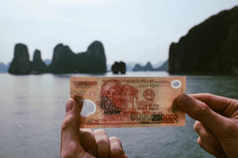 A person holding up a 200000 Vietnamese dong note with the coastline in the background.