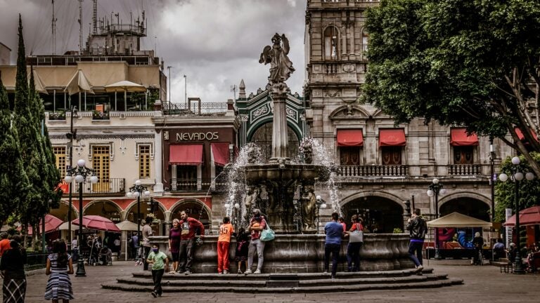 An overcast day in Zócalo, Mexico City's main square. People sit around a fountain.