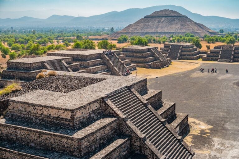 The ancient temples of Teotihuacan with tourists walking around the structures.