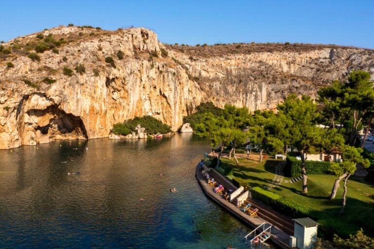 Lake Vouliagmeni, Greece and surrounding cliffs with tourists swimming.