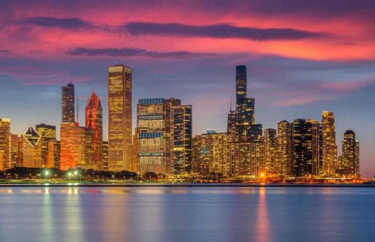 Las Vegas skyline filled with tall buildings lit up by individual lights against a purple sunset background

