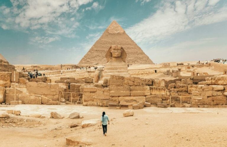 A person walking towards the great pyramids of giza, with the great sphinx in front of it 