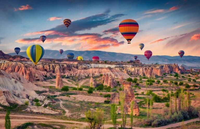 a rugged, white mountainous landscape with multi-colored hot air balloons against an evening sky