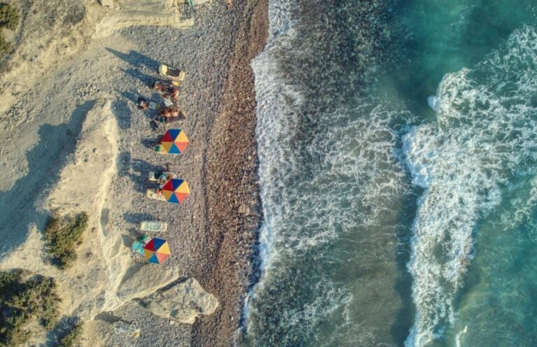 an aerial view of multi-colored umbrella and sun chairs in front of the ocean 