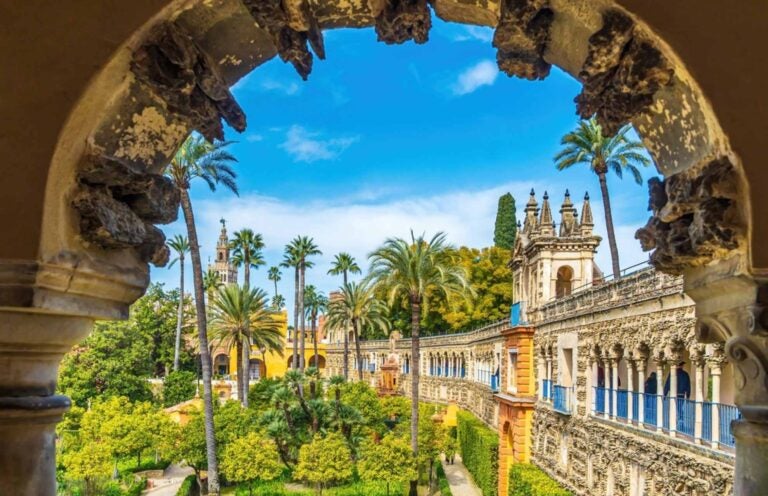 an ethereal, lush green garden filled with green foliage and palm trees and surrounded by intricately designed architecture 