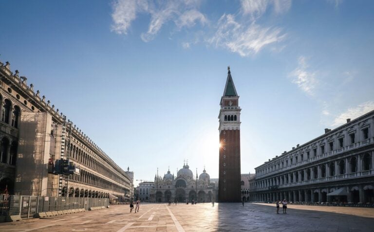 Saint Mark's Square early in the morning with the sun shining over the tiled floor with barely any people