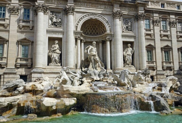 the ivory statues of the trevi fountain glisten in the sun against the turqouise water below