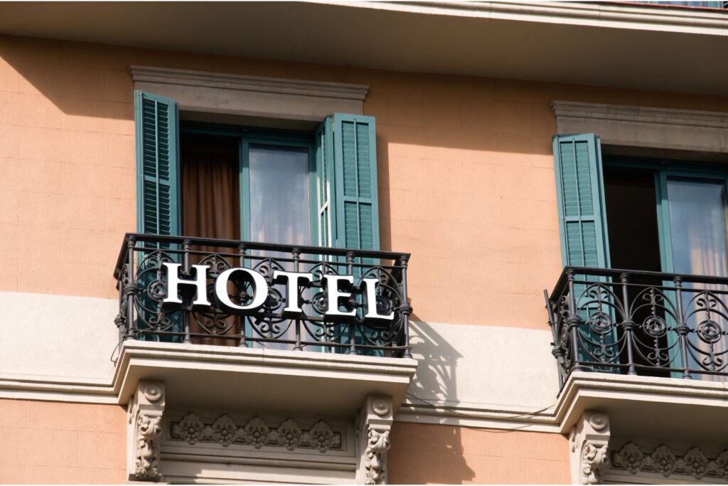 Closeup of two balconies with dark green shutters. One balcony is displaying a sign that says "hotel".