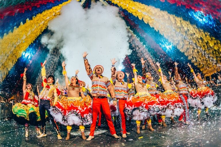 Celebrators dressed in colorful costumes in front of a colorful background during the Festa Junina festival, Rio.