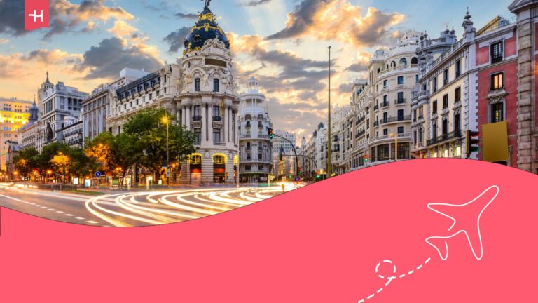 City of Madrid on a cloudy afternoon with lights from cars rushing by captured. Holafly log on the top left corner and an illustration of an aeroplane on the bottom right corner.