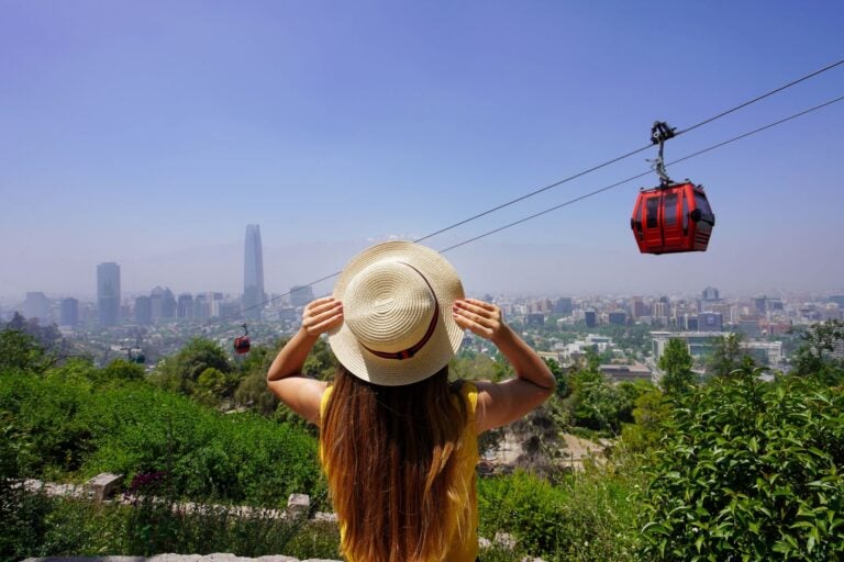 Woman with a white straw hat and long hair facing a descending cable car in the town of Valparaiso, Chile.