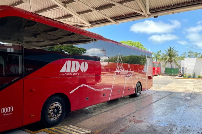 Side view of a red ADO bus stationed at an undercover bus terminal during the day.