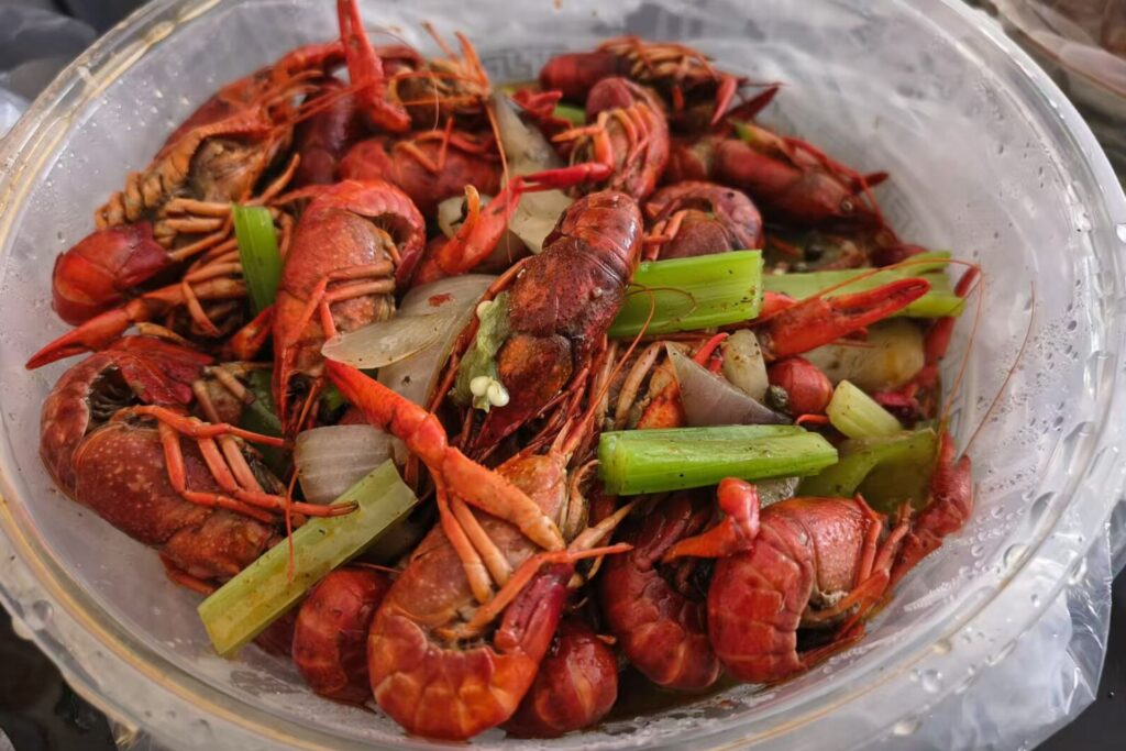 Boiled spicy crayfish dish in a plastic bowl, with green vegetables garnished on the top.