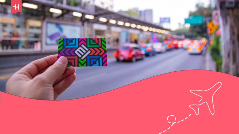 Person holding a metro card for Mexico City in front of a busy street with cars and buses passing by. Holafly logo on the top left corner, and an illustration of an aeroplane on the bottom right corner.