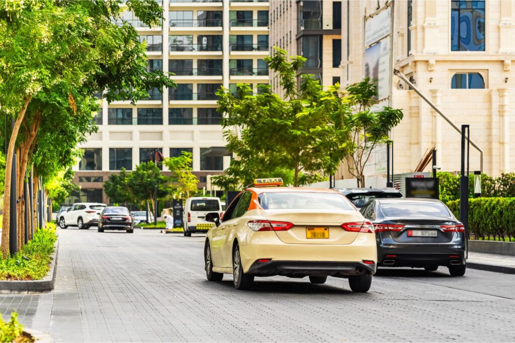 Dubai city street with a view of the back of a taxi and other cars. buildings and trees are surrounding the street with the cars driving on it.