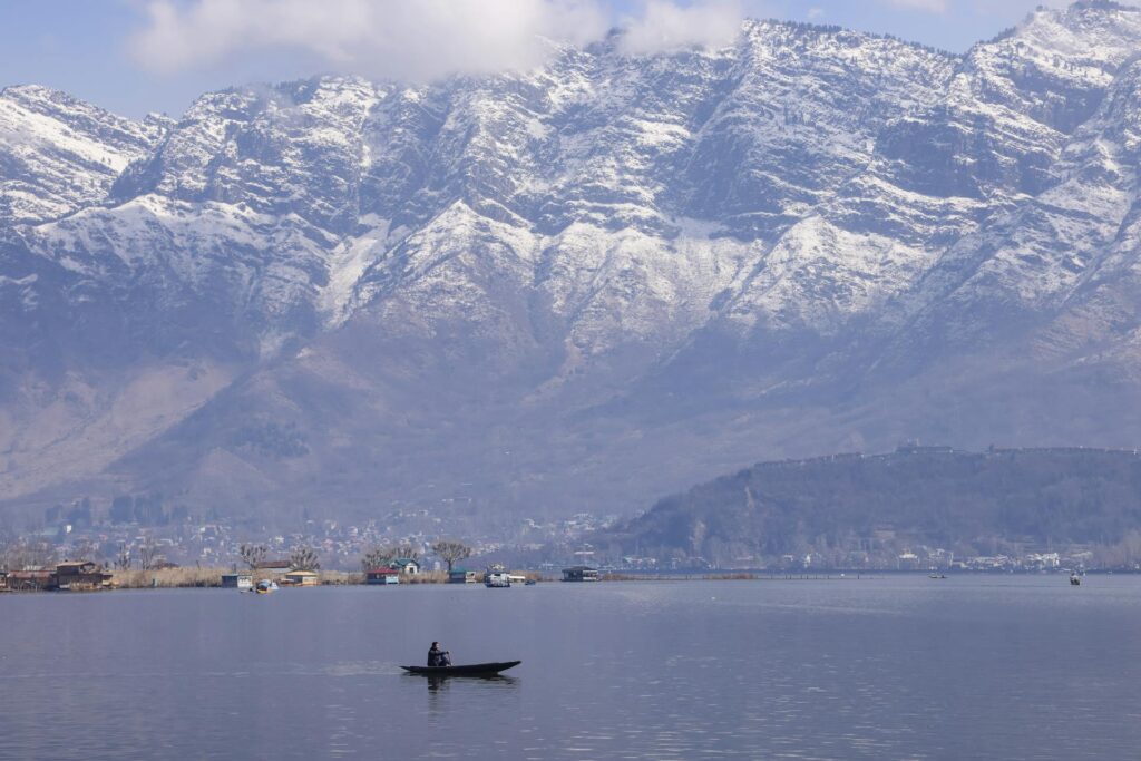 Man riding a boat in the Dal Lake with snowy mountains in the background