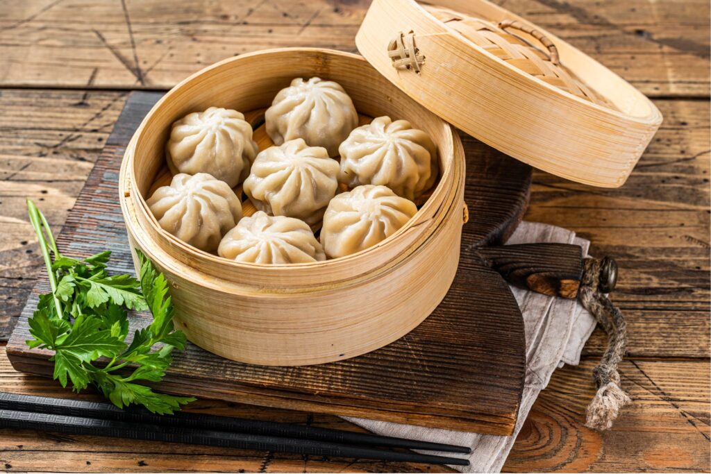 Pork buns are displayed in a bamboo bowl atop a wooden board, with a parsley stem on the side.