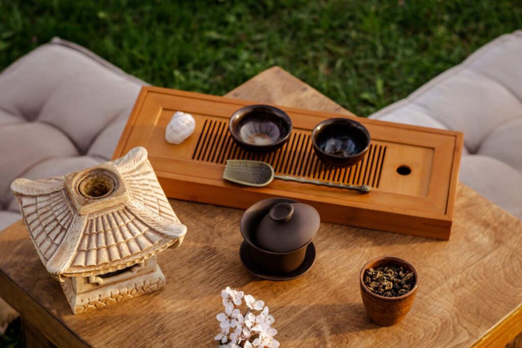 Wooden table on grass with beige cushions and traditional ceramic tea set on top of the table.