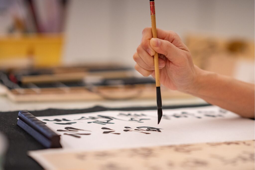 A hand painting Chinese letters on a white piece of paper.