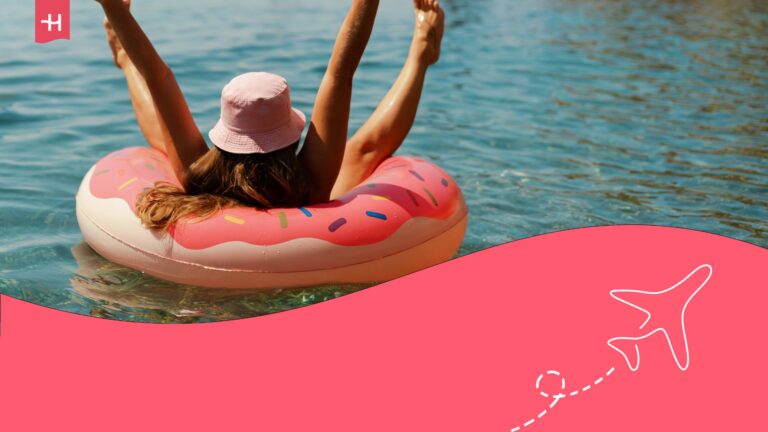 A woman with a straw hat and her arms raised in a lake on a doughnut-shaped floating accessory.