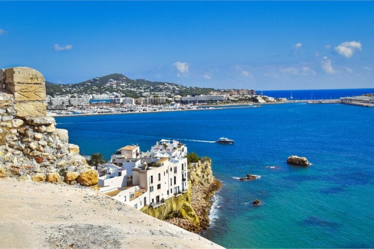 The city of Ibiza, surrounding ocean and boat sailing along the water.
