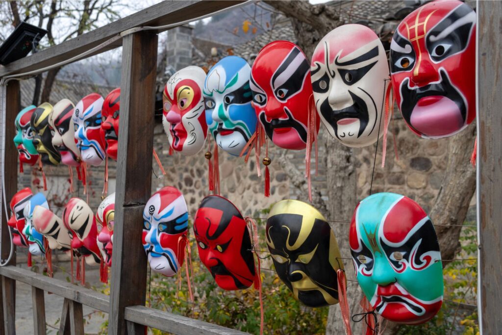 Two rows of vibrant coloured masks hanging on an outdoor wooden panel.