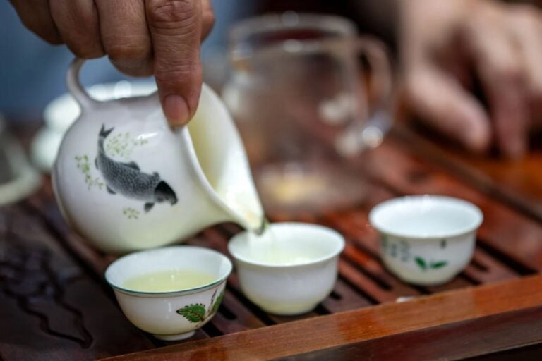 Close-up of three tea cups and tea kettle, on a wooden tray.