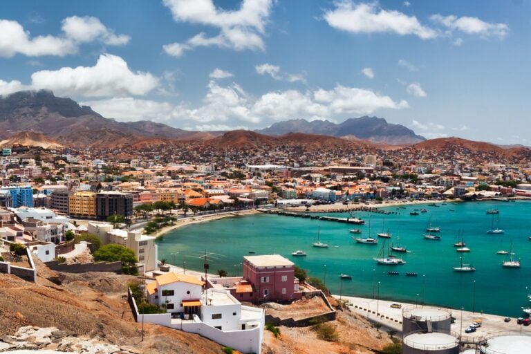 View of Cape Verde's shoreline, with boats anchored near the shore, surrounded by houses and mountains.