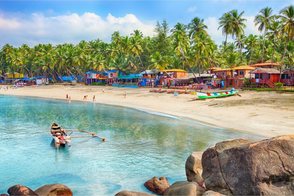 Shoreline of the Arabian Sea in a town in Goa, with colourful houses and boats along the shoreline and in the water.