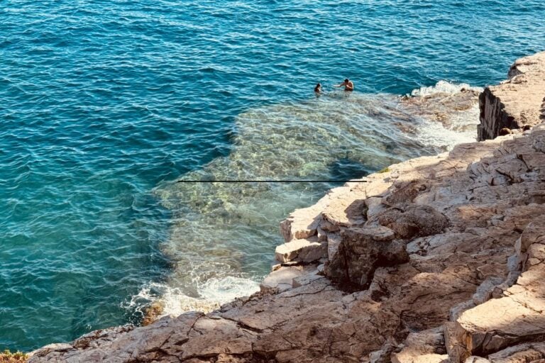 Close-up of the beaches of Pula, with two people swimming in the water.