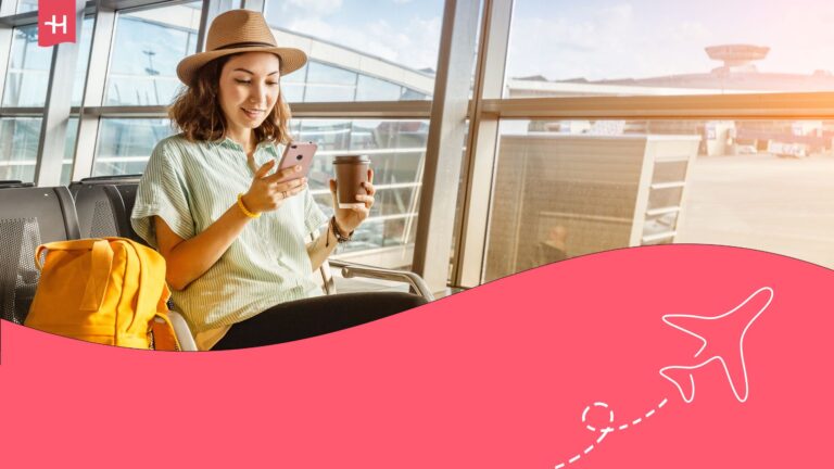 Woman sitting in an airport lounge with a yellow backpack beside her, holding a cell phone in her right hand, and a coffee in her left hand.