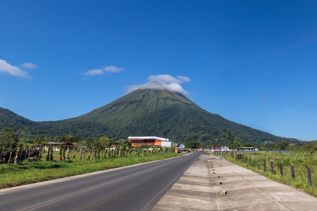 A volcano in the background of a small town and a road leading into it.