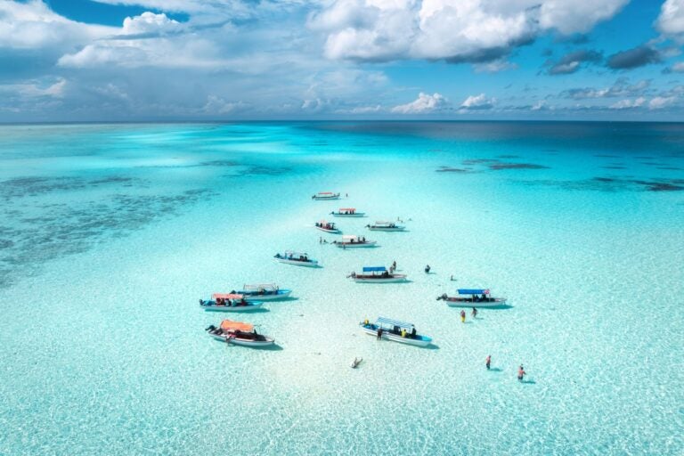 Aerial view of the water surrounding the island of Zanzibar, and boats and fisherman dotted along the water.