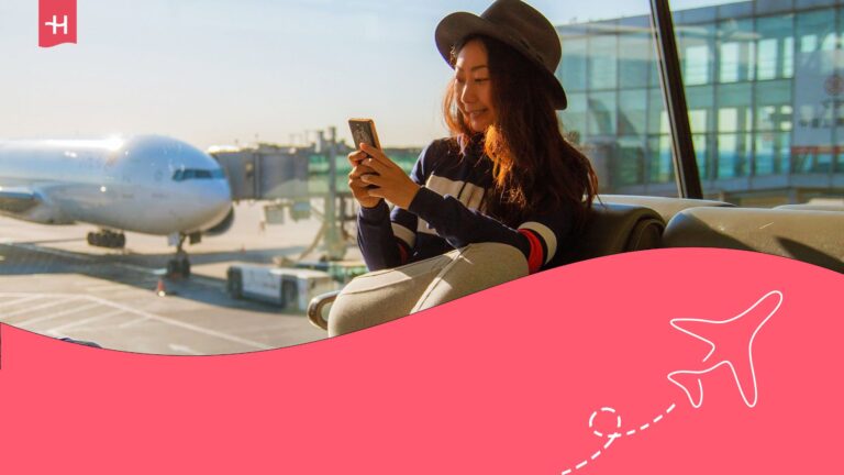 A woman in a black hat is sitting at an airport lounge with her feet up. She is holding a mobile phone, and behind her is an aeroplane.
