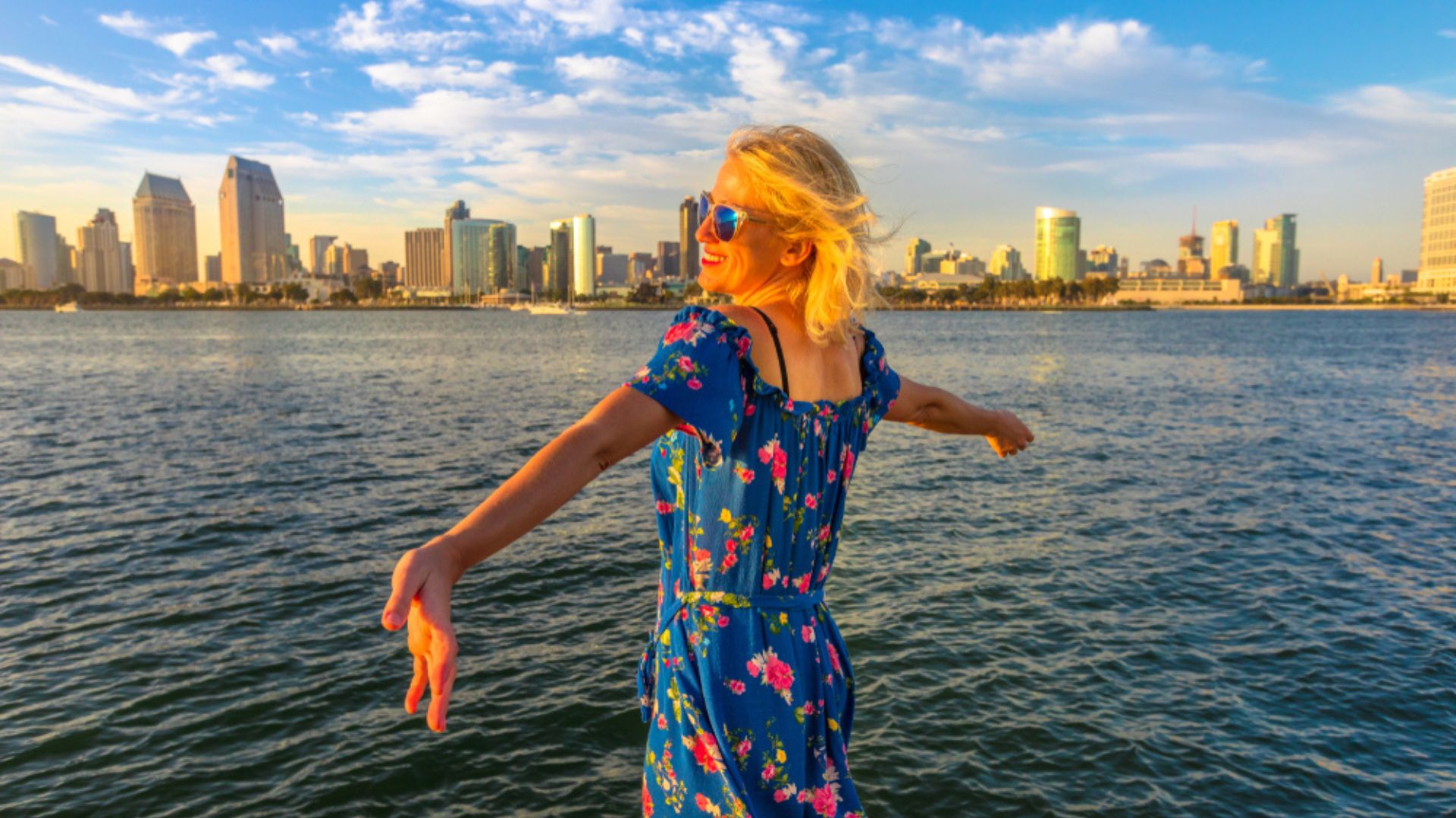 A woman with outstretched arms looks at the San Diego skyline