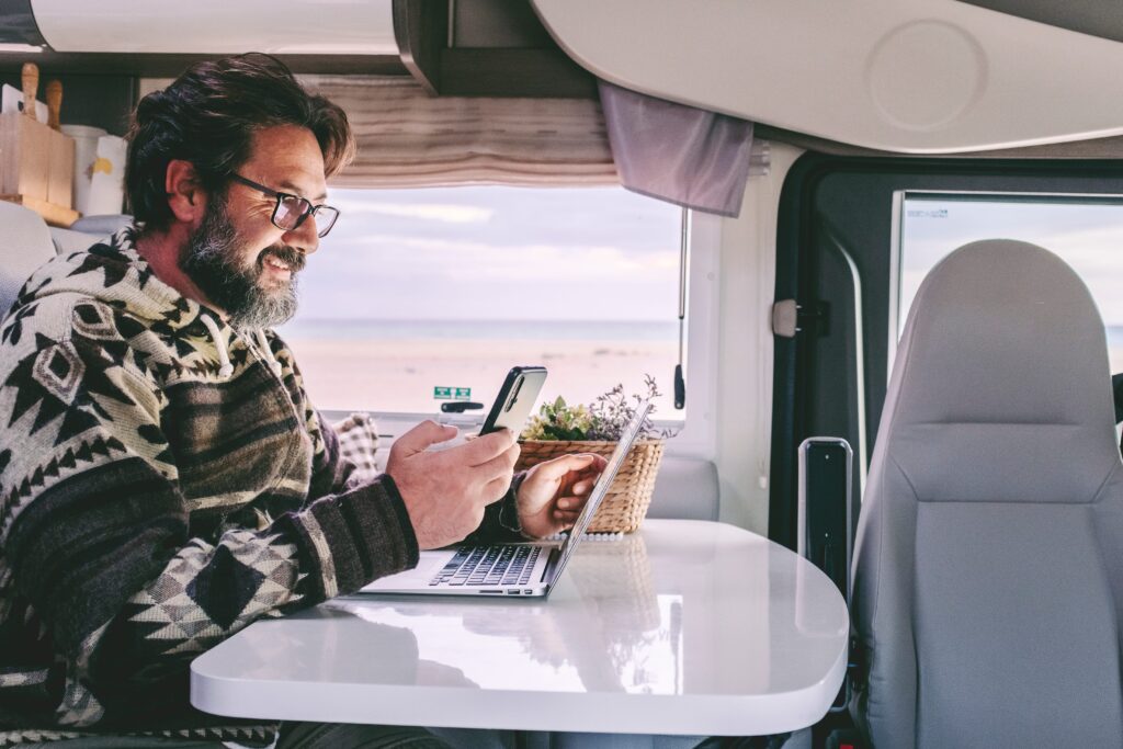 A man is working on a train with his laptop and mobile phone. 