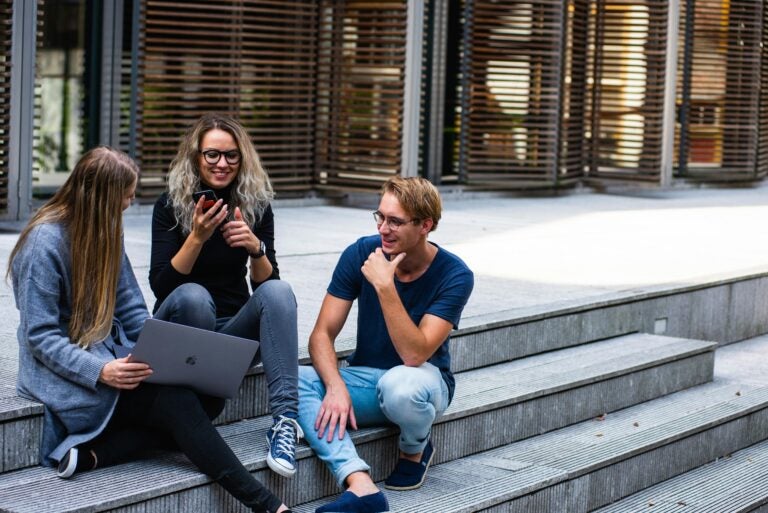 Three students sitting on outdoor steps, using best collaborative apps for students to work on an assignment.