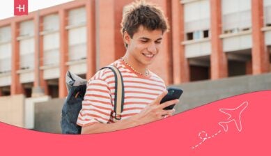 student at his university, looking at his phone and smiling - Midwest Student Exchange Program