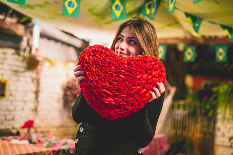 Young pretty girl hiding behind a heart pillow in a brazilian restaurant in background