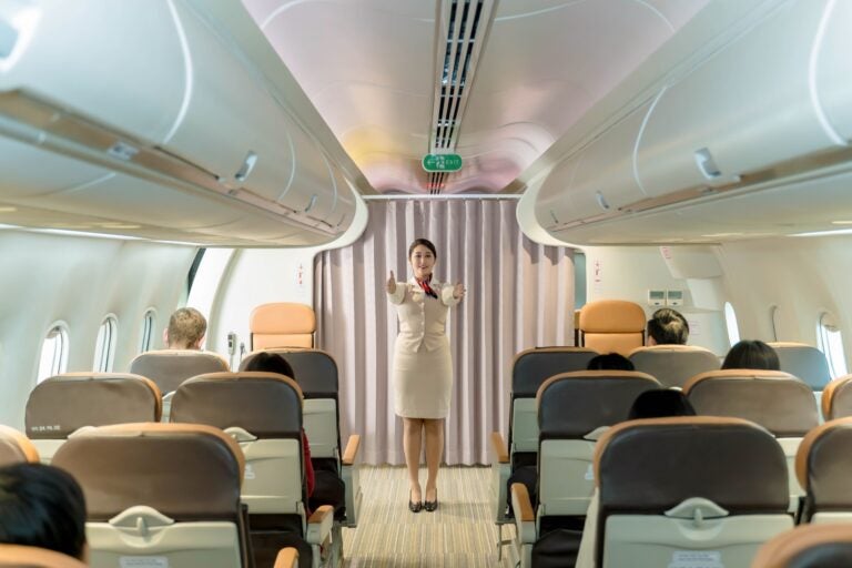 A flight attendant from the best flight attendant school in Canada is giving instructions to passengers before take-off.