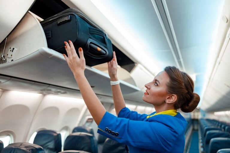 Flight attendant arranging an overhead luggage.