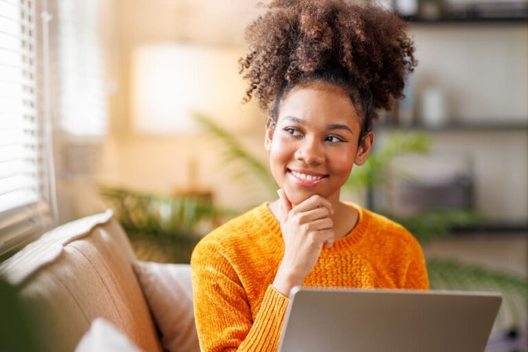 African American woman with Afro hair studying at home using a laptop, serious expression while thinking about a question, looking confused.