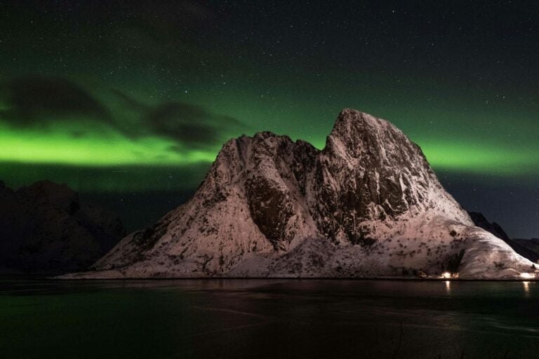 Aurora Borealis glowing green over a snowy mountain at night.
