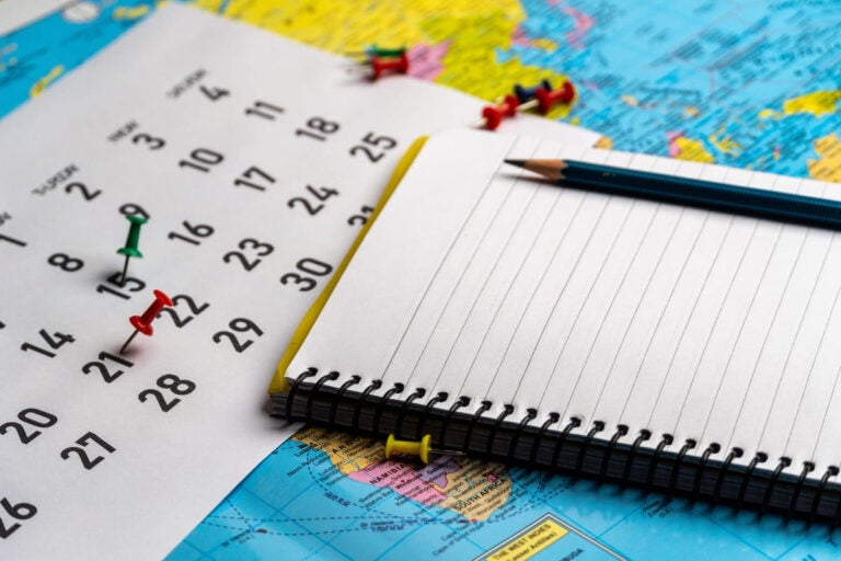 Push-pin in calendar with a blank notebook and pencil.