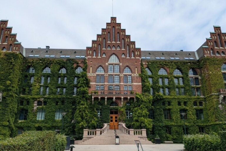 A grand brick building with Gothic windows covered in green ivy.