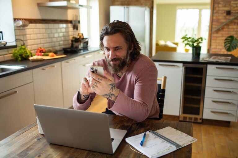 Young adult man using a smartphone in the kitchen while working from home.