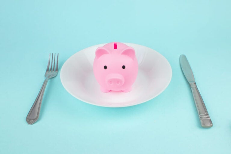 Piggy bank on a plate with fork and knife representing daily food and travel expenses in Bahrain